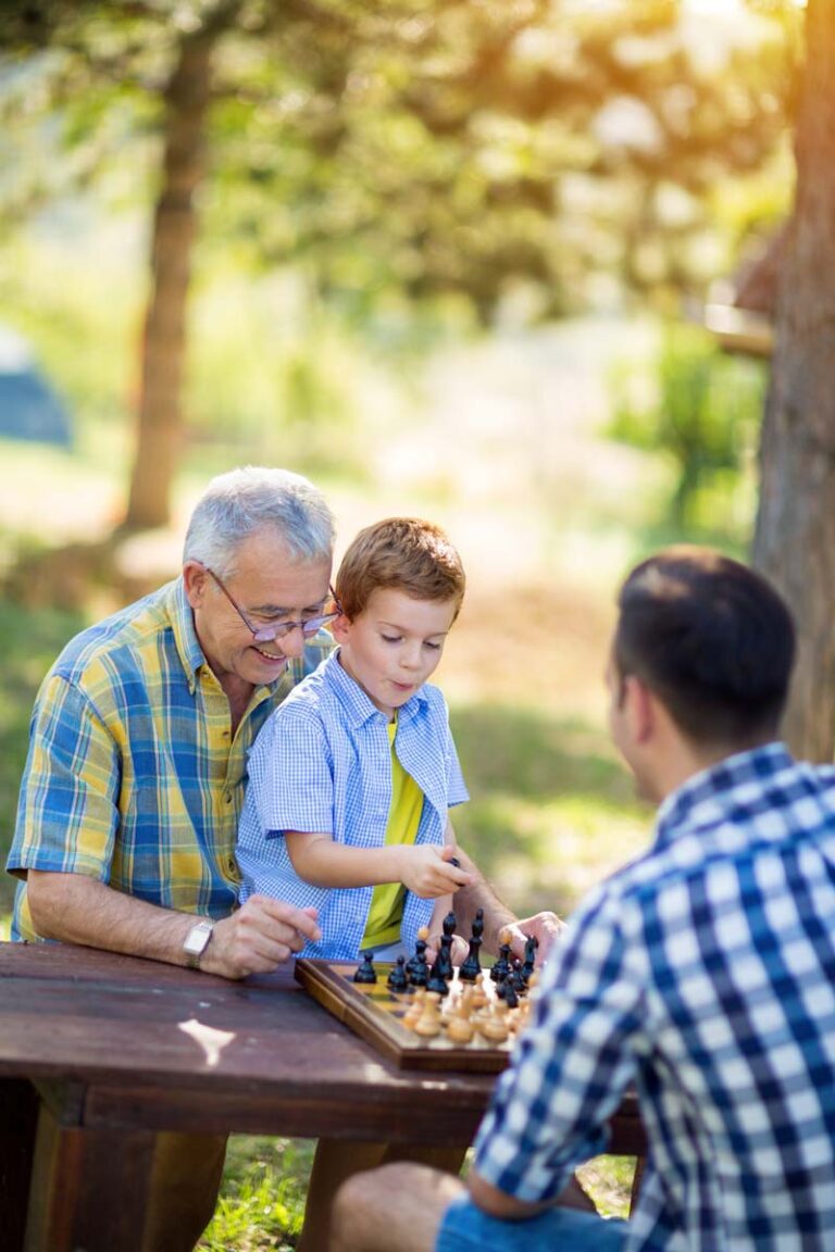 Proveer at Byrd Springs | Senior man playing chess outside with visiting family members